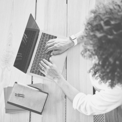 A person with dark curly hair types on a laptop.
